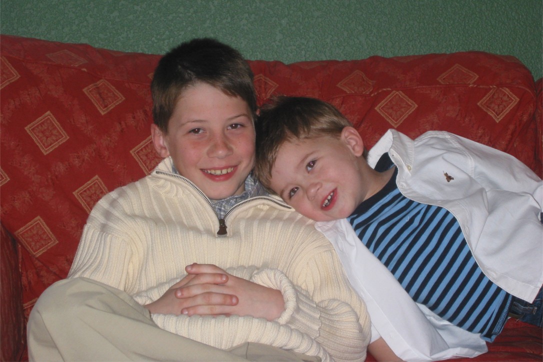 Two young brothers grinning side by side on a red patterned couch