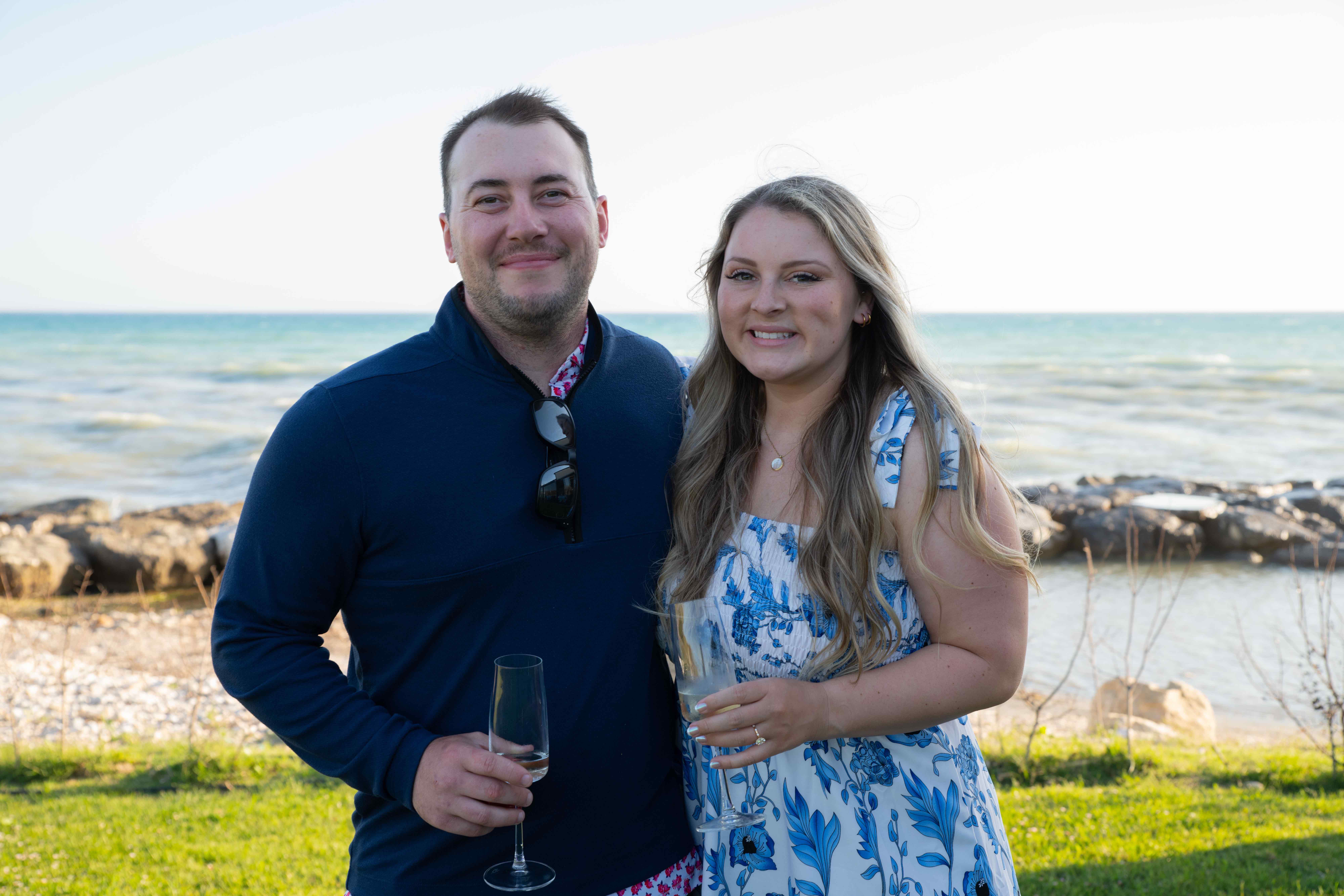 A young couple with drinks on the rocky lakeshore in golden-hour light